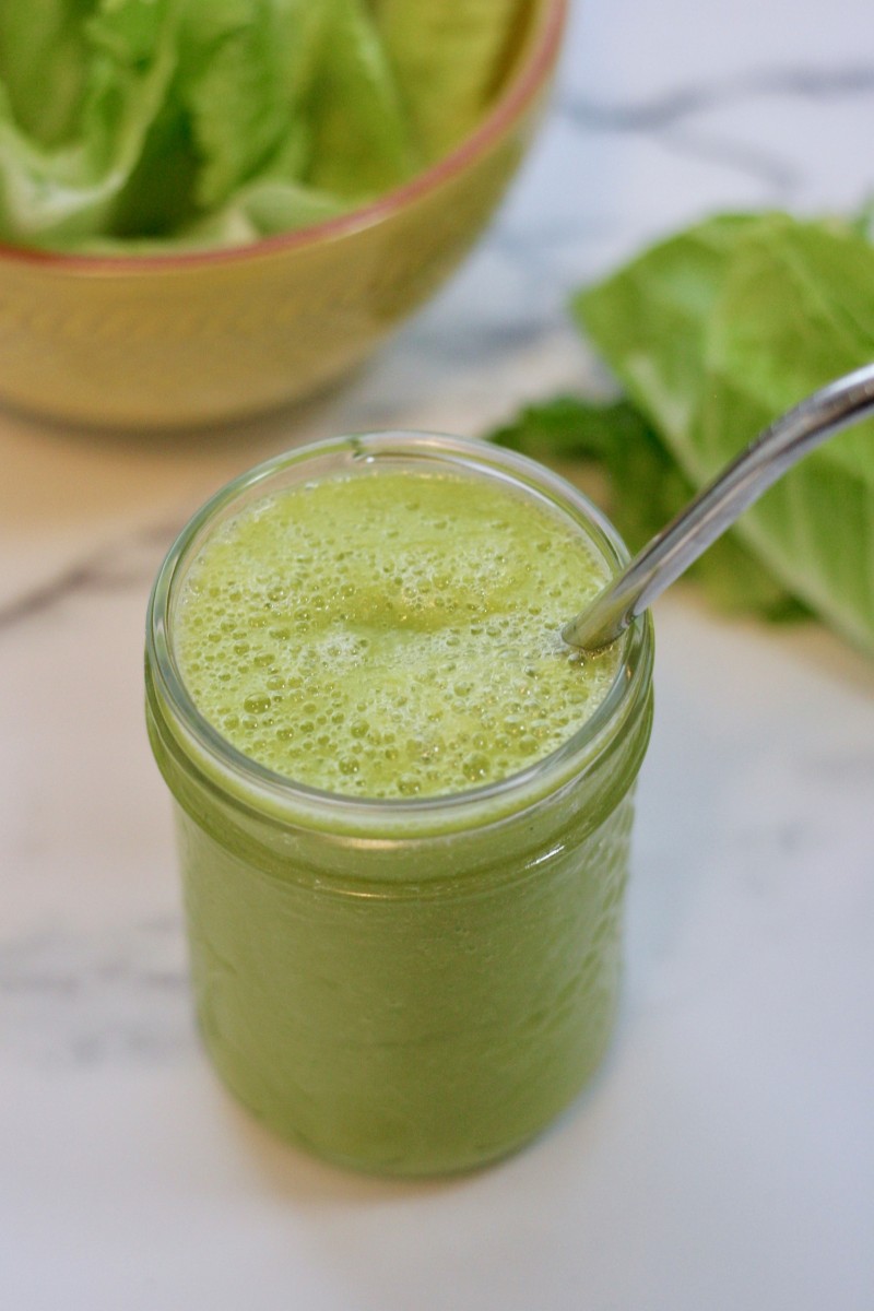 A green smoothie in a small mason jar with a stainless steel straw.