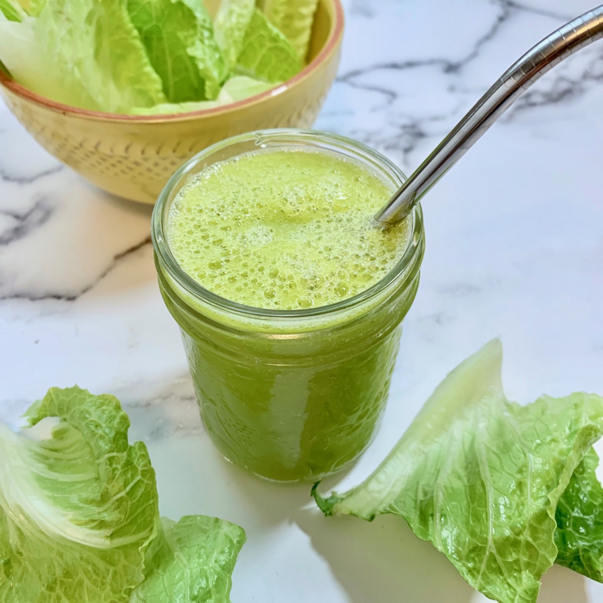 A green smoothie in a small mason jar with a stainless steel straw.