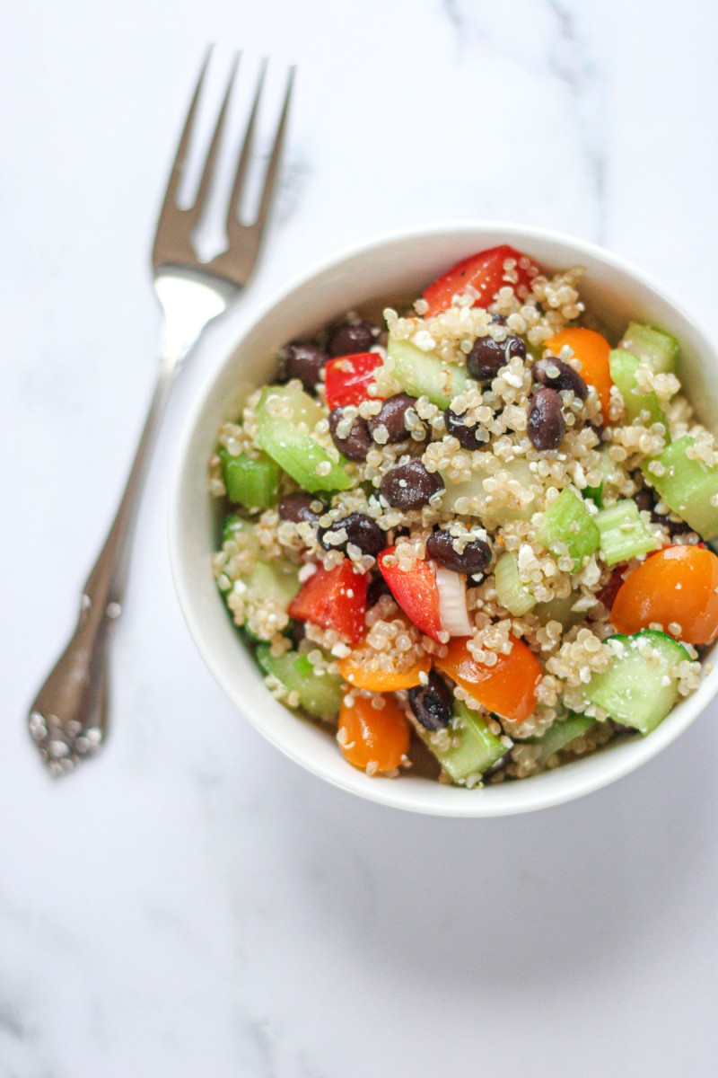 A small white bowl filled with quinoa black bean salad with a fork beside.