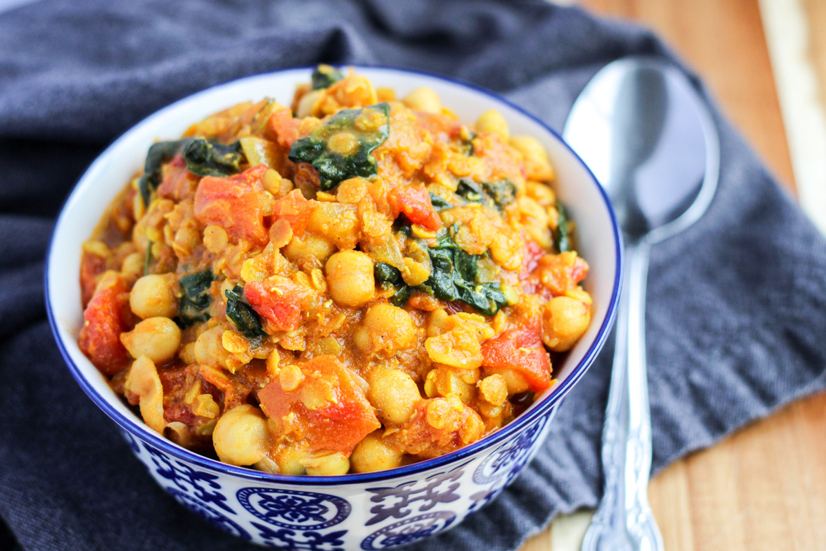 A small blue bowl filled with Red Lentil and Chickpea Curry with Spinach with a silver spoon beside