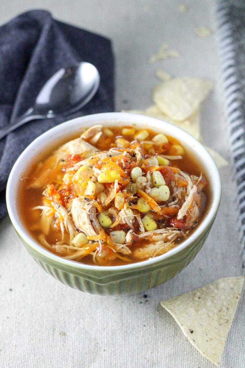 A small bowl of Chicken Tortilla Soup on a tan placemat with tortilla chips on the side