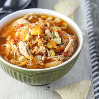 A small green bowl of Healthy Insta Pot Chicken Tortilla Soup on a off-white placemat