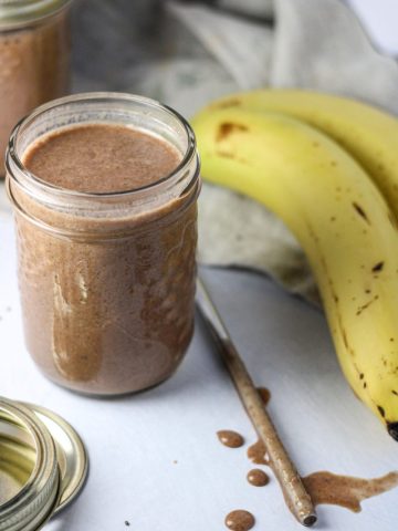 A small mason jar Banana Date Chia Smoothie with a metal straw beside it