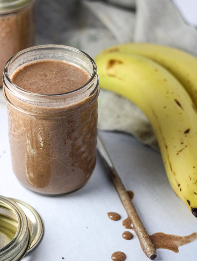 A small mason jar Banana Date Chia Smoothie with a metal straw beside it