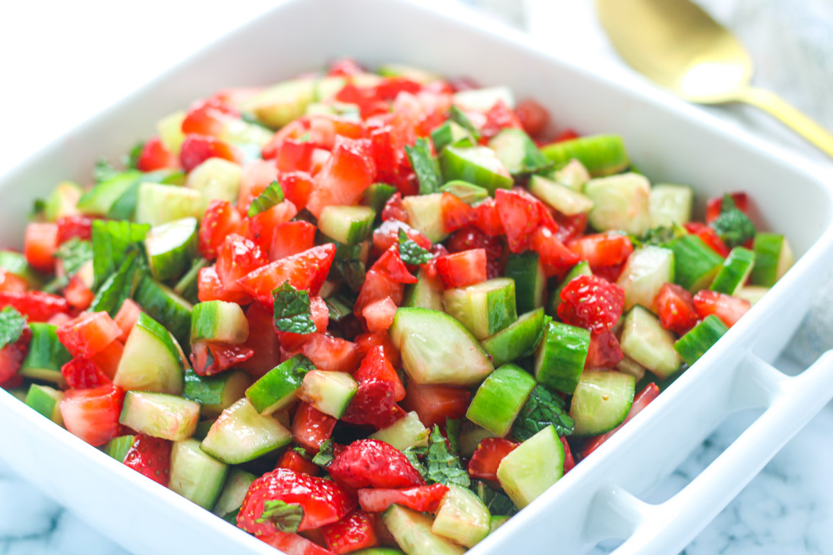 A square white serving dish filled with chopped strawberry Cucumber Salad with Mint