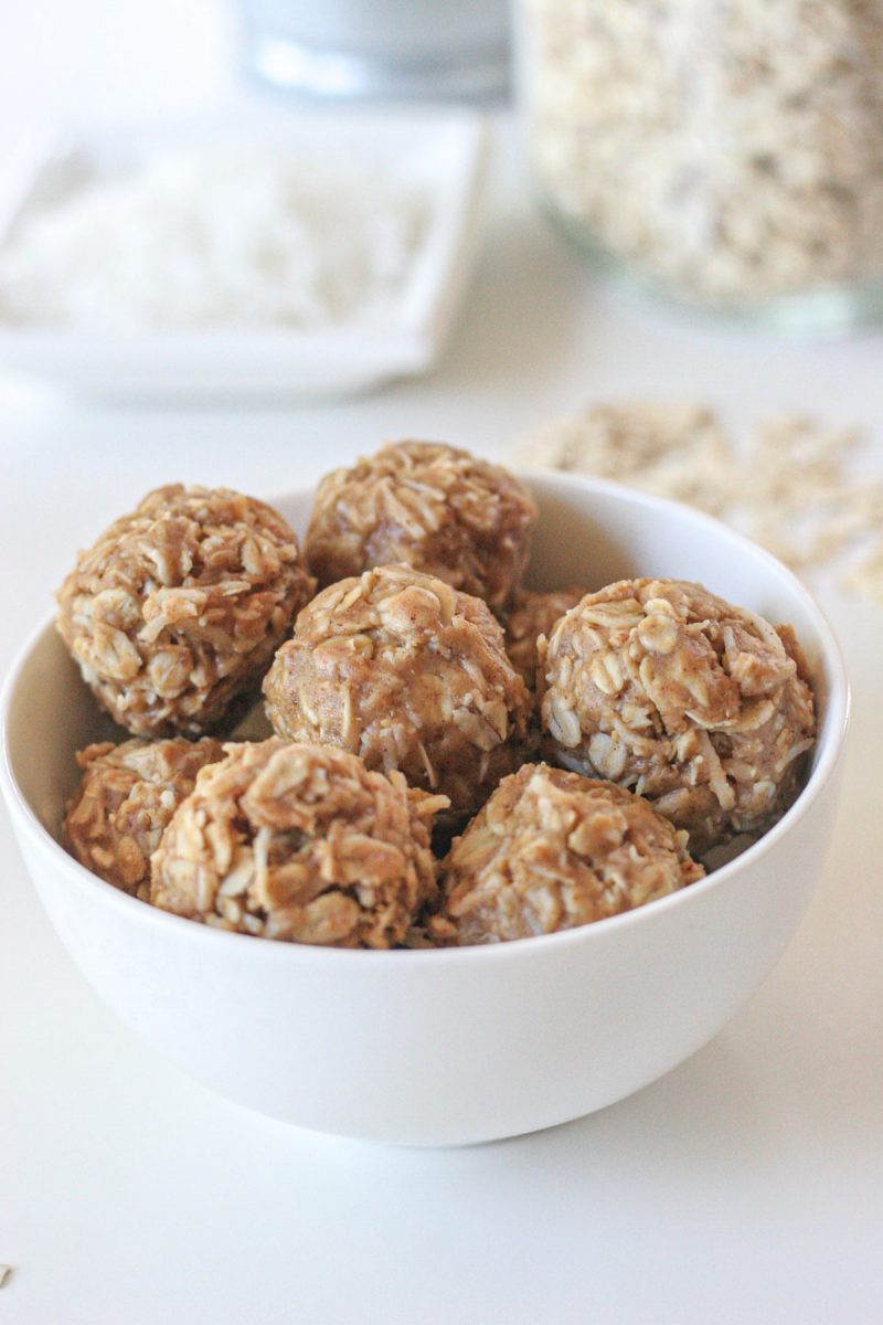 A white bowl of coconut and peanut butter energy bites on a white table.