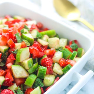 A white dish filled with strawberry Cucumber Salad with Mint with a gold spoon