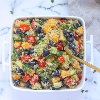 A white dish of Summer Quinoa Salad with Mango and Blueberries with a gold spoon in it