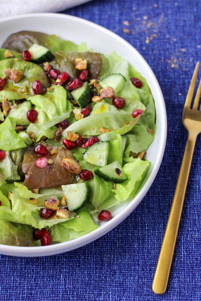 A white plate filled with Butter Lettuce and Pomegranate Salad on a blue tablecloth
