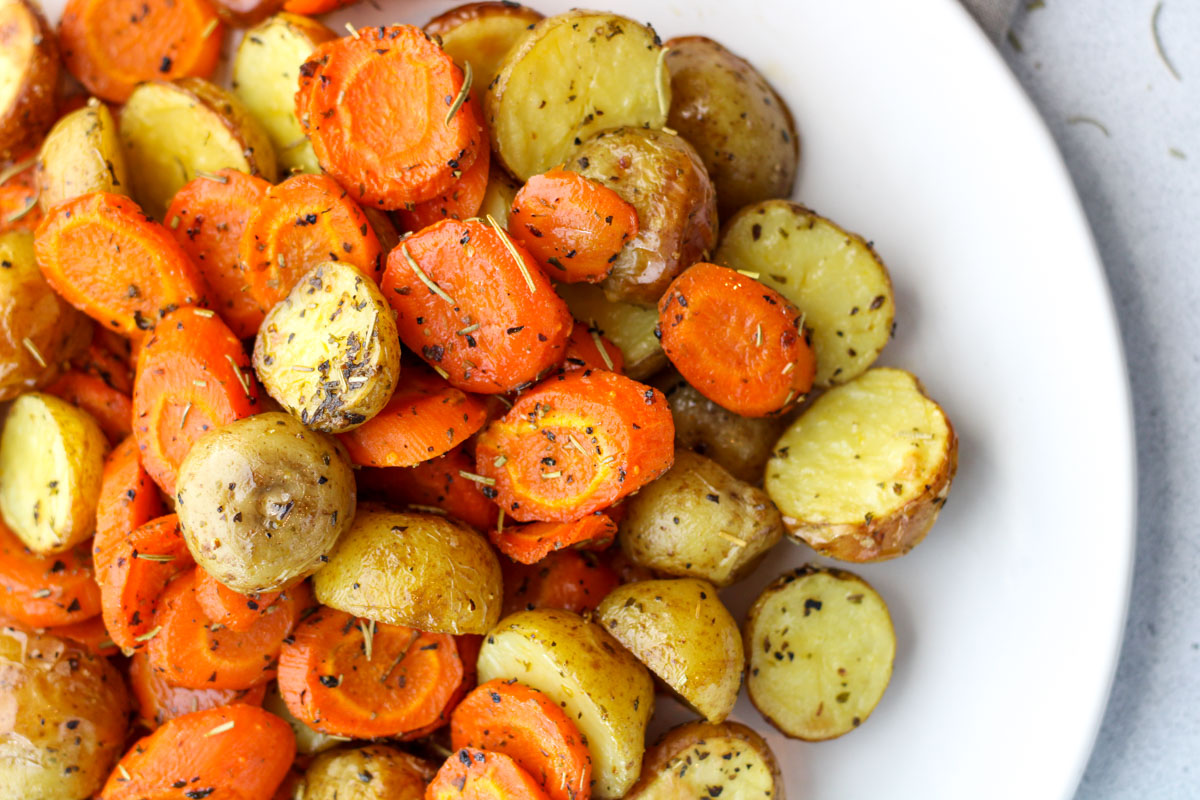 A white plate filled with roasted Potatoes and Carrots.