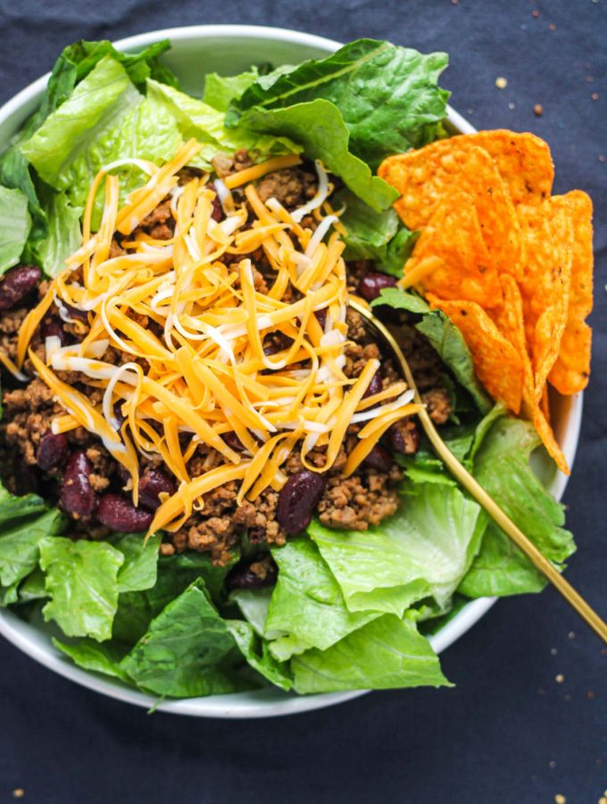 A white plate filled with romaine lettuce ground beef and kidney beans topped with shredded cheese