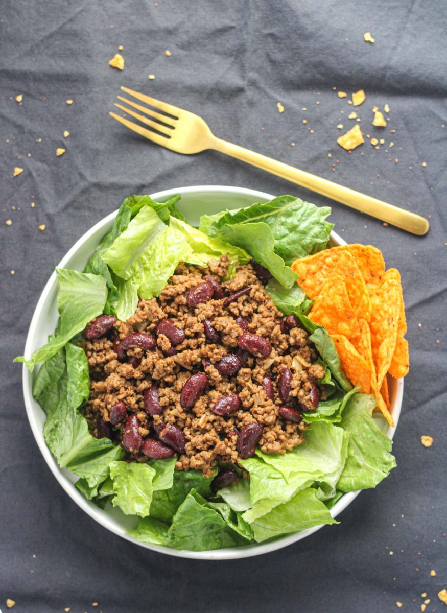 A white plate on top of a grey tablecloth filled with romaine lettuce and ground beef mixture