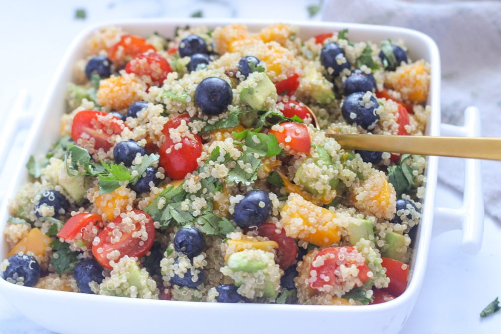 A white serving dish of quinoa, blueberries, mango and cherry tomatoes
