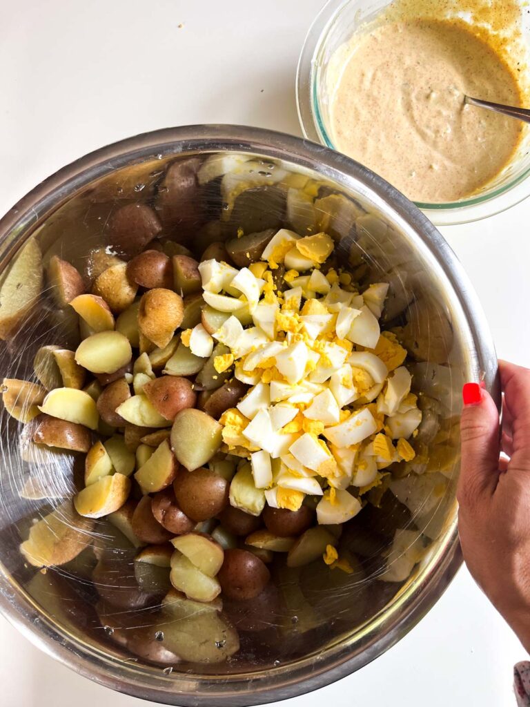 A large bowl with hard boiled eggs, potatoes and dressing.