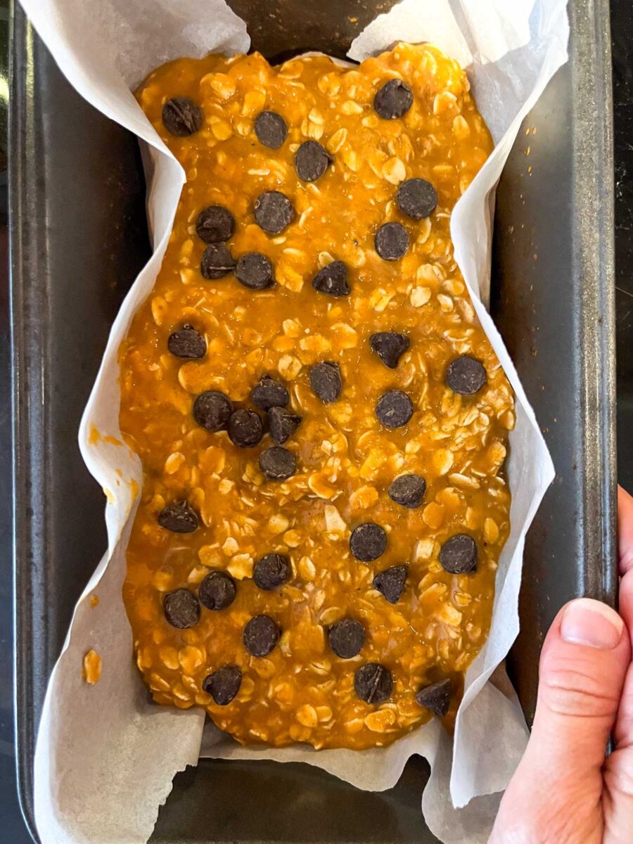 Chocolate chips on top of pumpkin baked oats batter in a loaf pan.