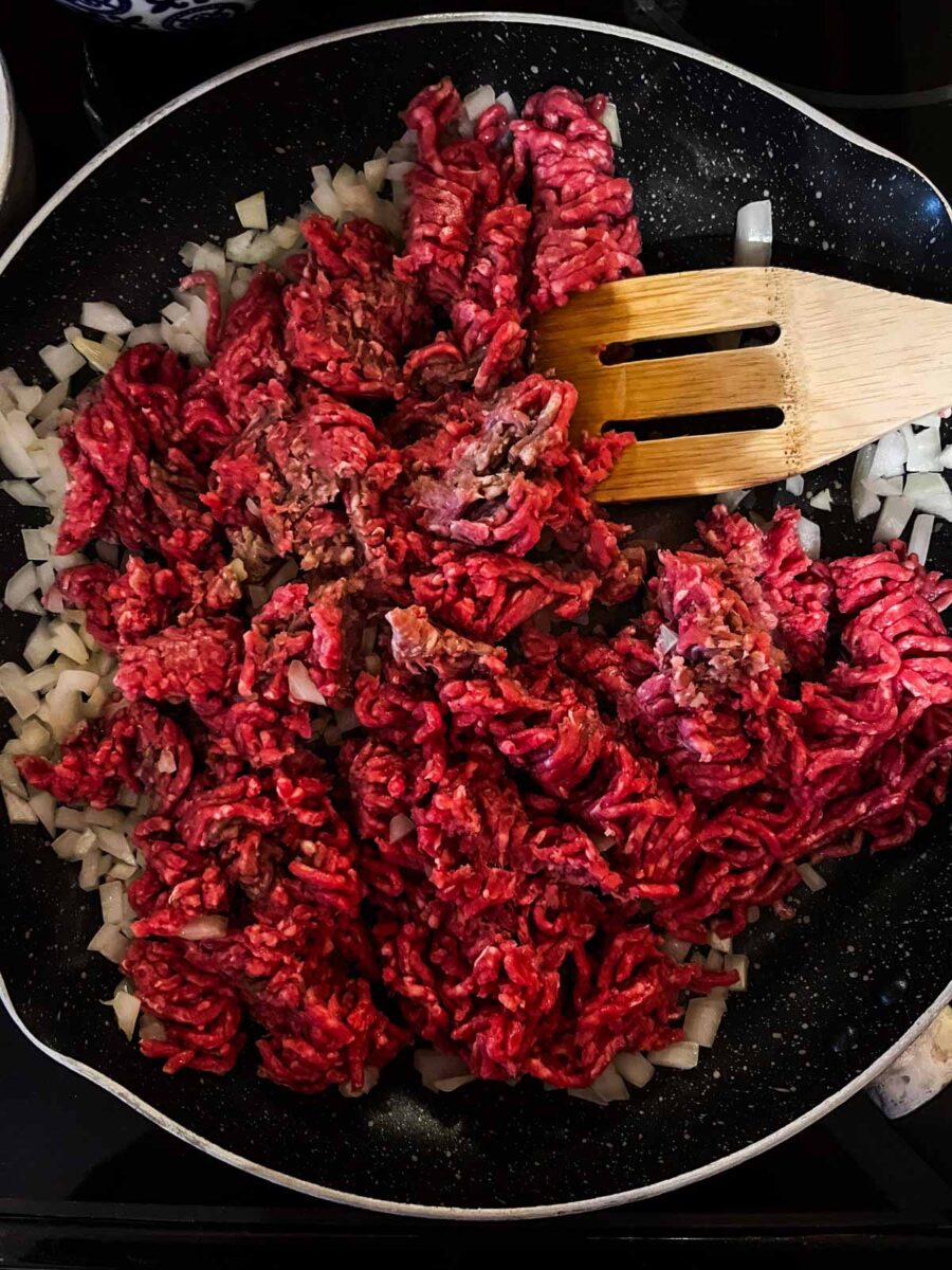 Ground beef in a pan with chopped onion.