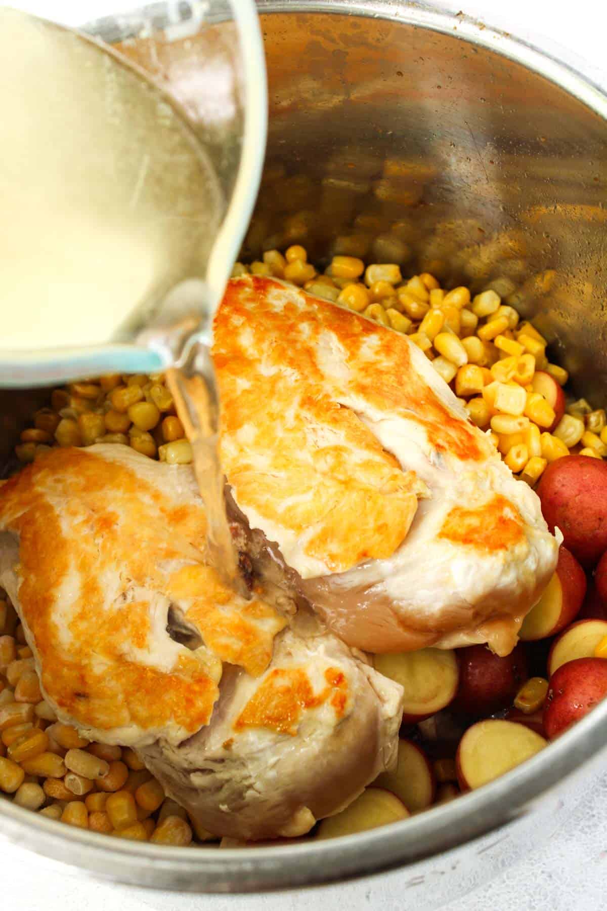 Pouring chicken stock overtop of chicken breasts and corn in a pot.