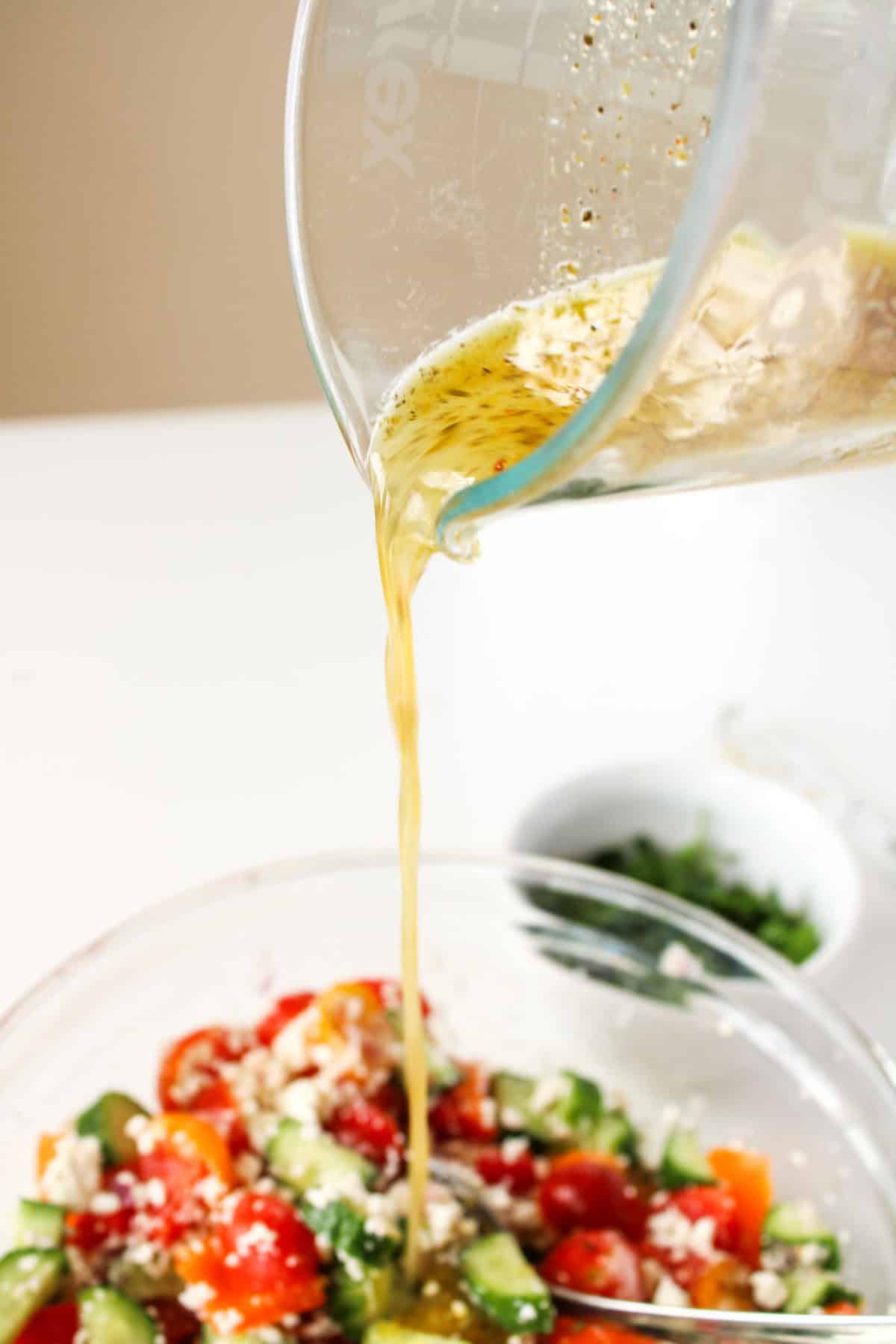 Pouring salad dressing over Greek salad.