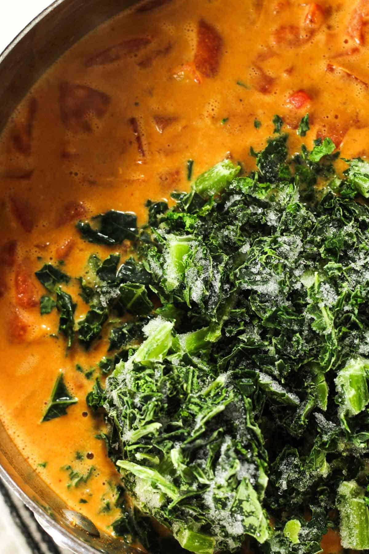 Adding frozen kale to the pot of curry.