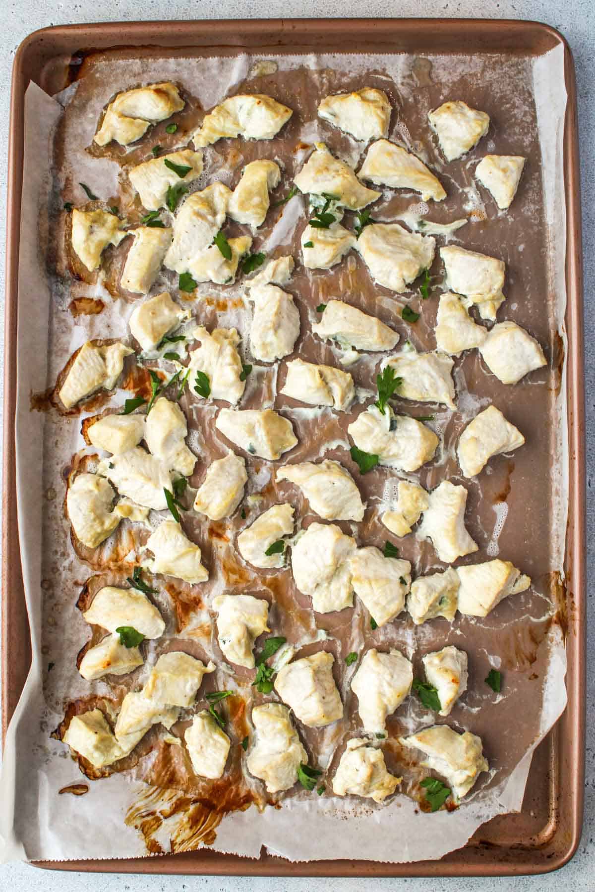 A large baking tray with cooked tzatziki Chicken Breast chunks on it.