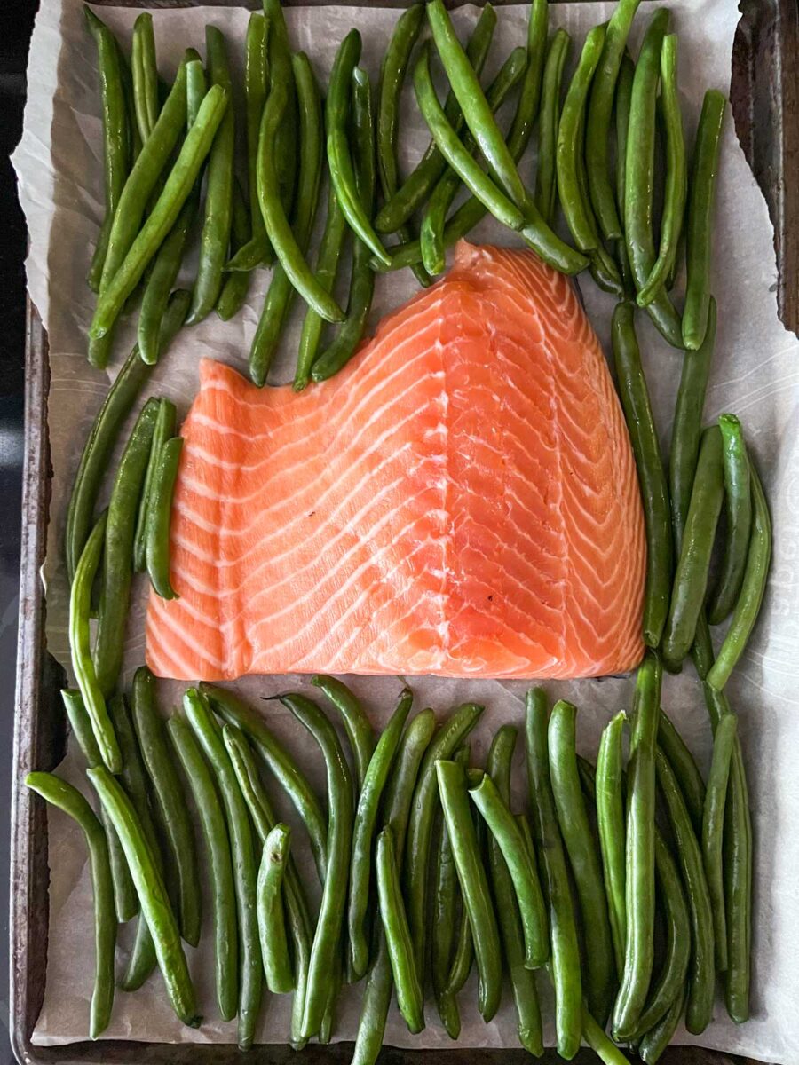 Salmon fillet and green beans on a baking sheet.
