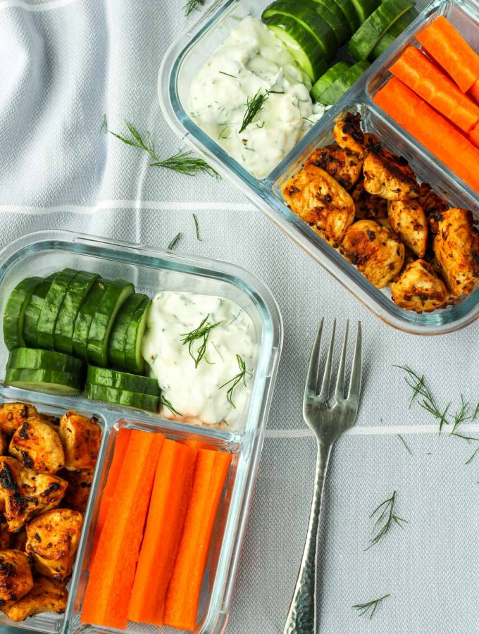 Bento box style glass containers with veggies, chicken and greek dip