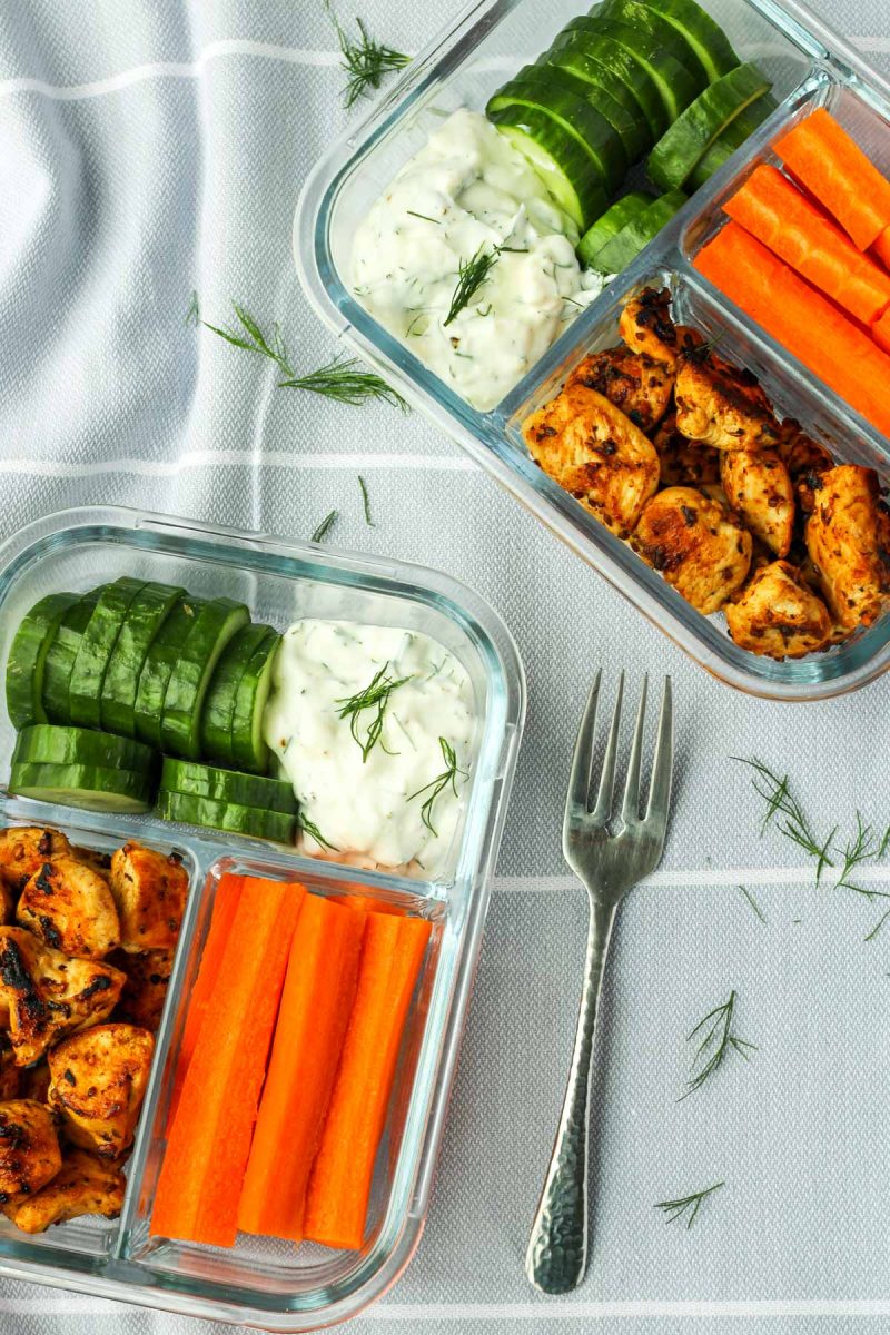Bento box style glass containers with veggies, chicken and greek dip