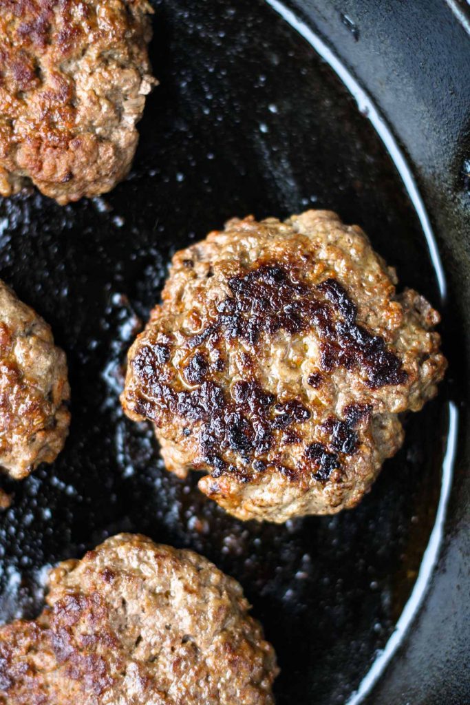 Cast iron skillet with cooked burger patties.