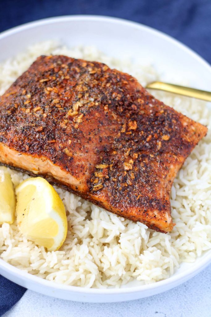 A piece of cajun salmon on a bed of rice with lemon.