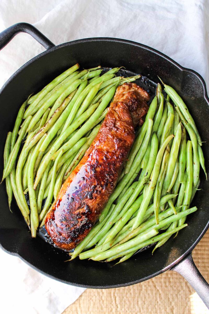 Cast iron porkloin in skillet with green beans.