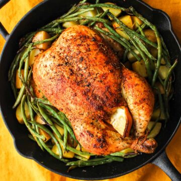 A cooked chicken in a cast iron skillet with green beans.