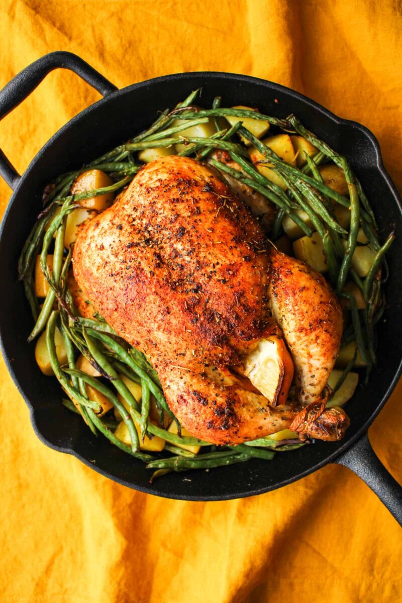 A cooked chicken in a cast iron skillet with green beans.