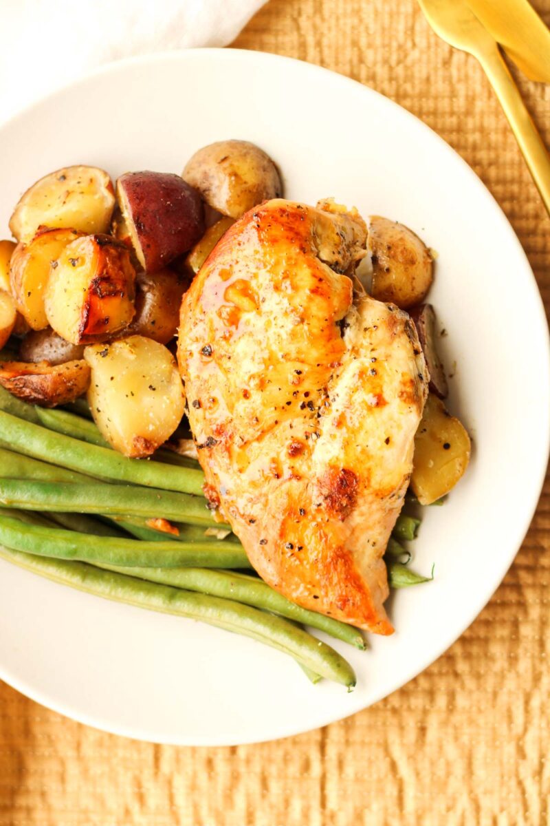Slow cooked chicken on a white plate with potatoes and green beans.