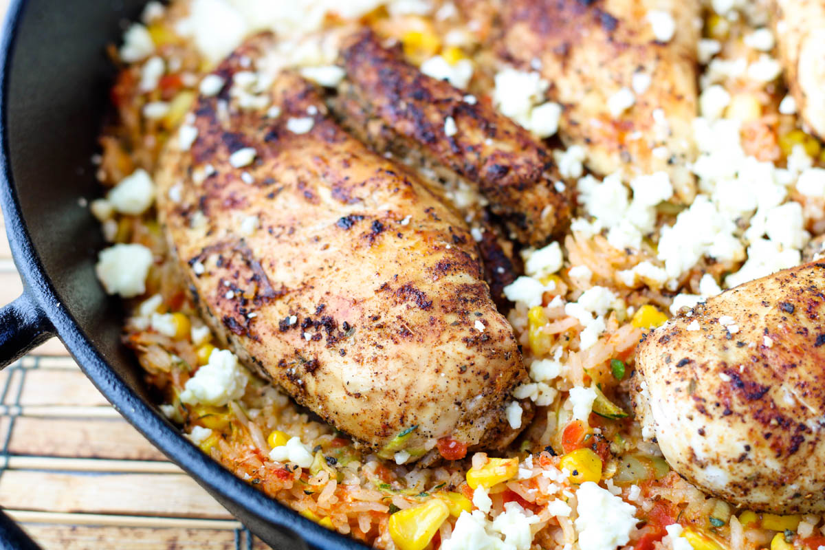 A cast iron pan filled with chicken breasts and rice.