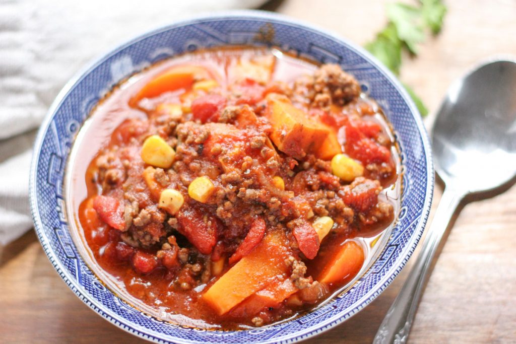 Close up of Easy Weeknight Hamburger Soup with Sweet Potatoes in a blue bowl with a silver spoon beside it