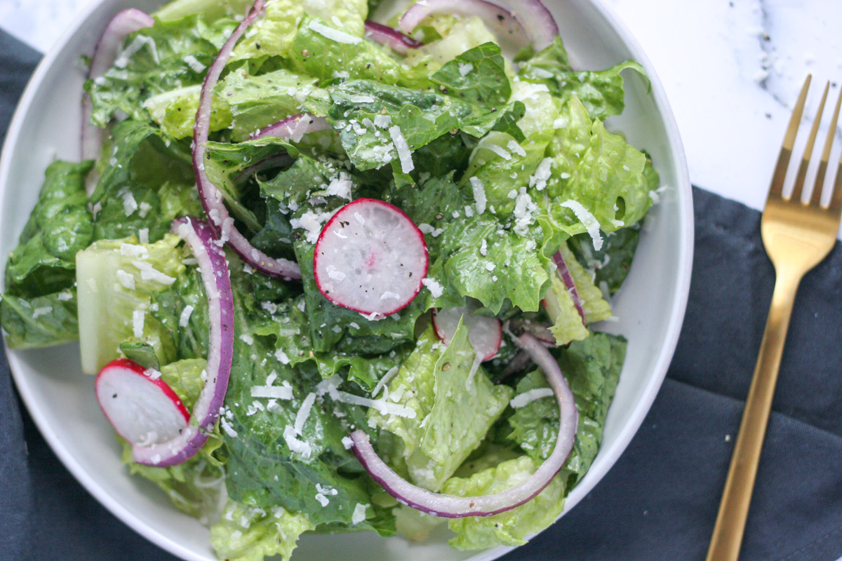 Close up of Simple Romaine Salad with Radish and Parmesan on a white plate with a gold fork