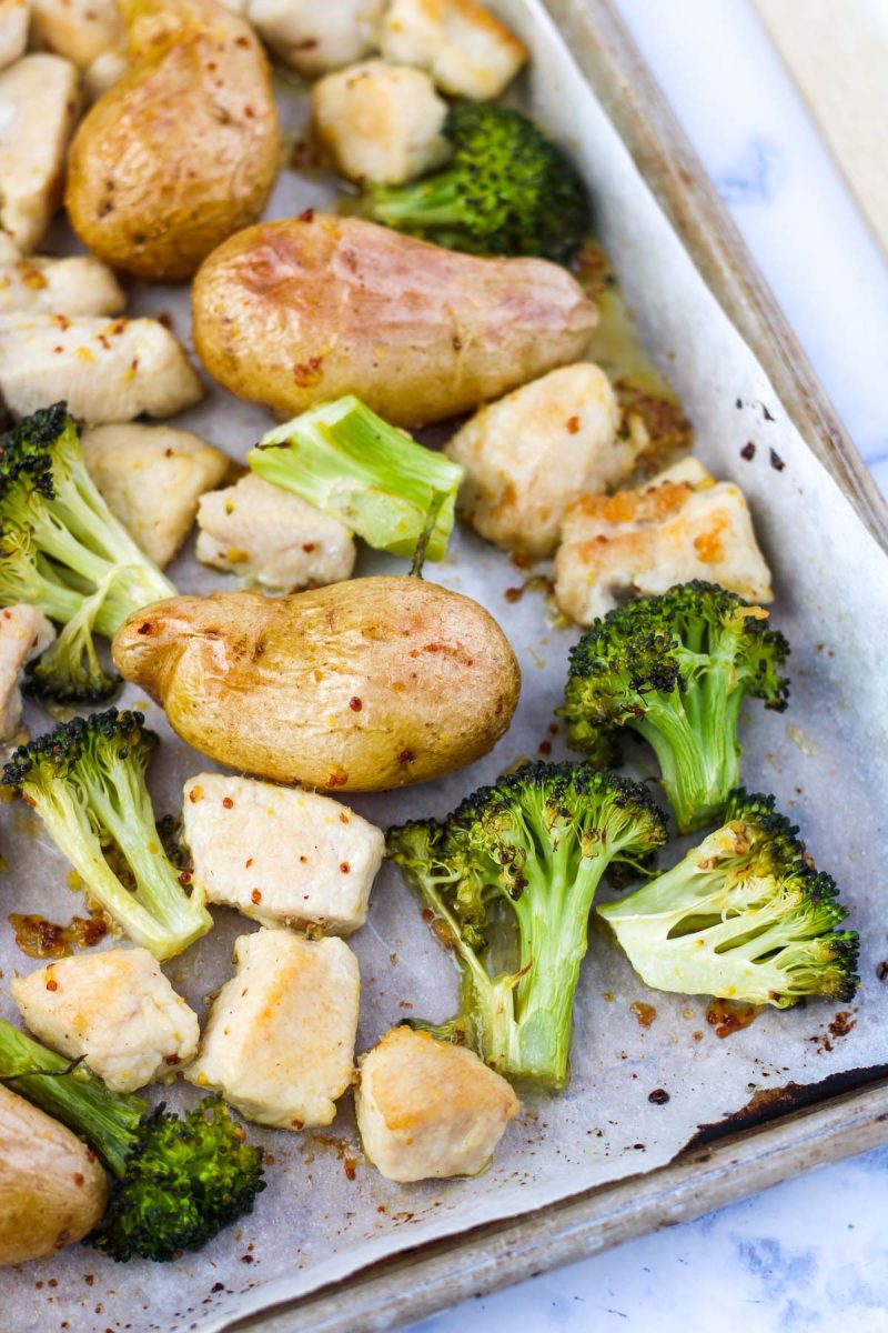 Close up of potatoes, broccoli and chicken on a baking sheet
