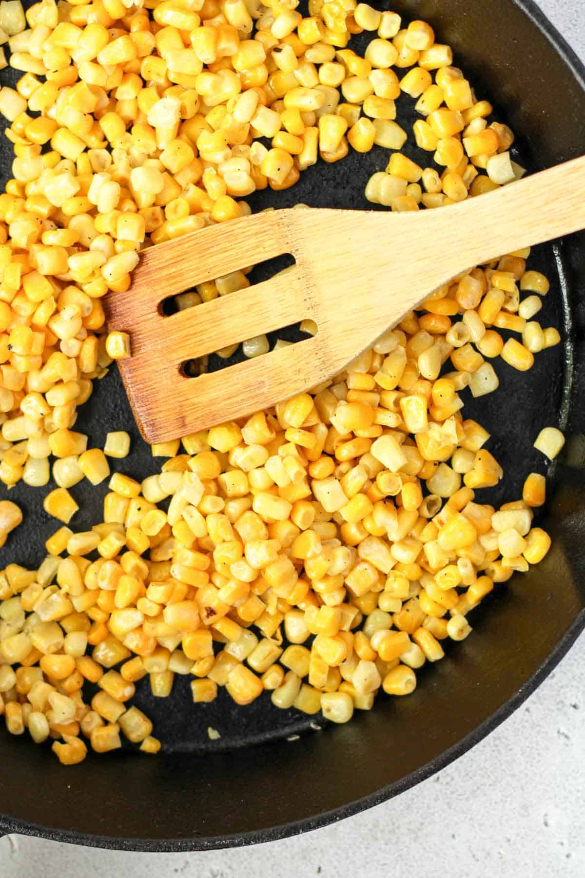 Corn kernels being cooked in a cast iron skillet.