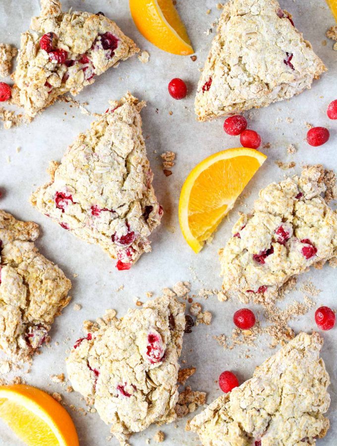 a parchment covered baking sheet with cranberry oatmeal scones and orange slices