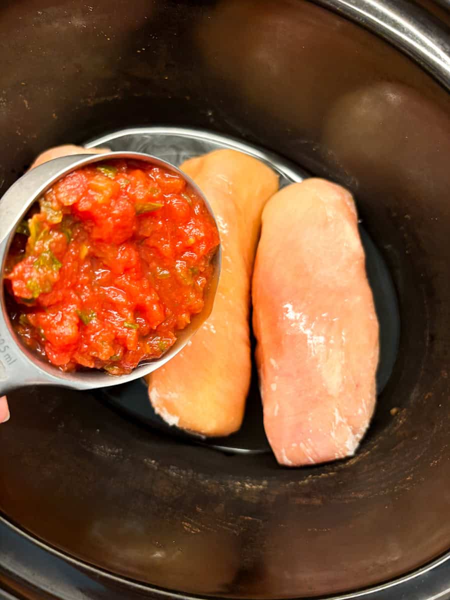 Putting salsa on frozen chicken breasts in a slow cooker.