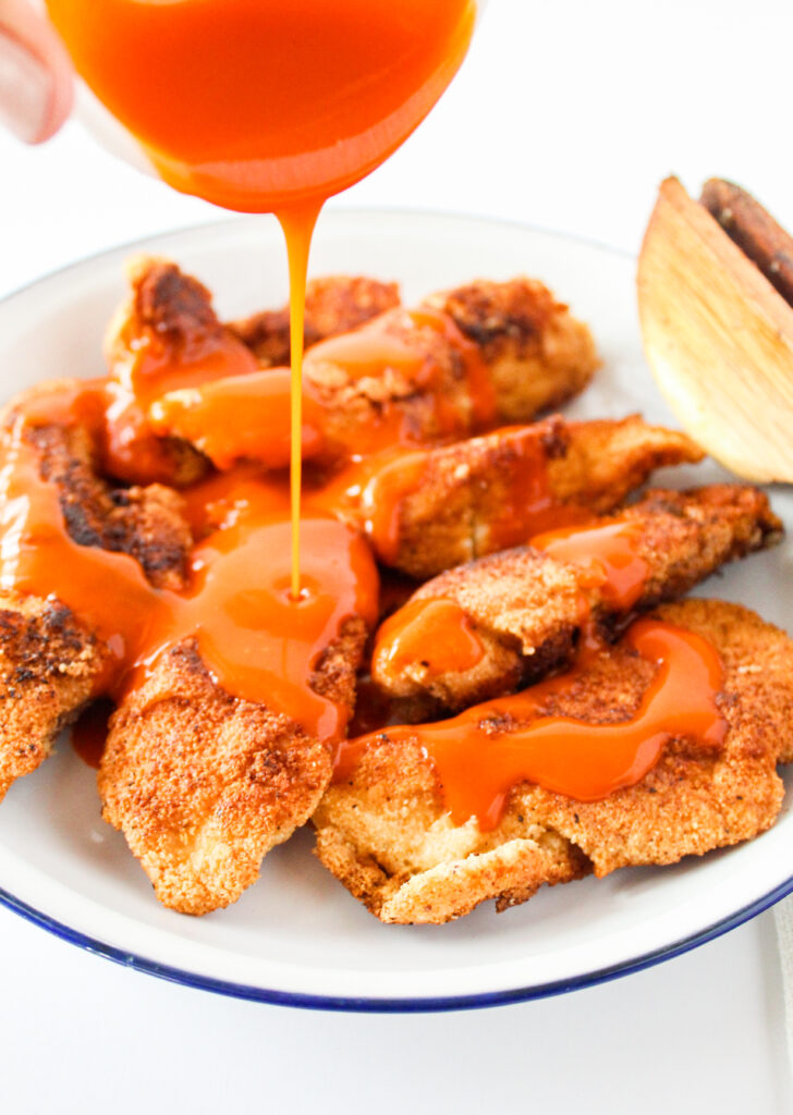 Pouring hot sauce over cooked chicken cutlets.