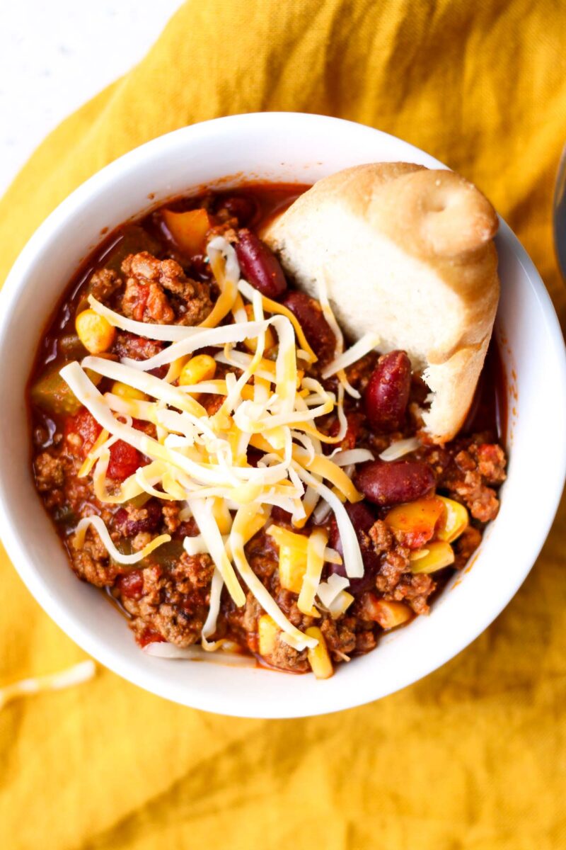 Chili topped with cheese in a white bowl with some gluten free bread.