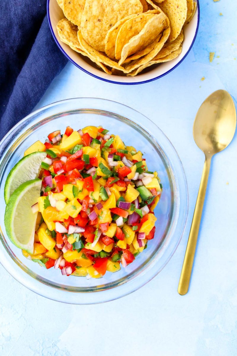 A glass bowl of mango salsa with a gold spoon beside.