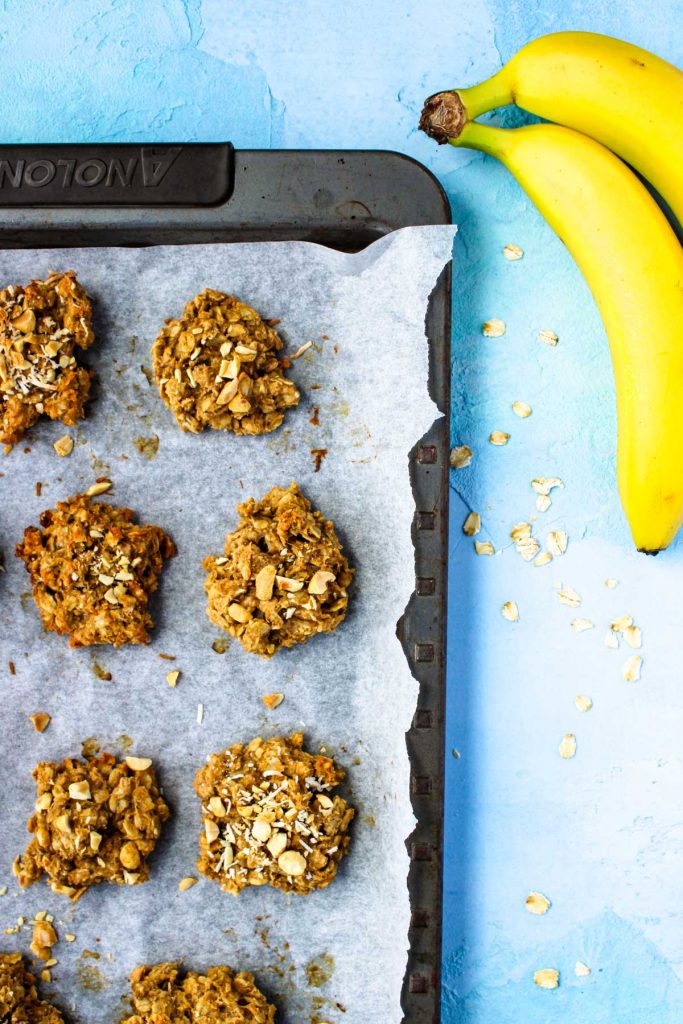 a cookie sheet with healthy peanut butter oat cookies with 2 bananas beside