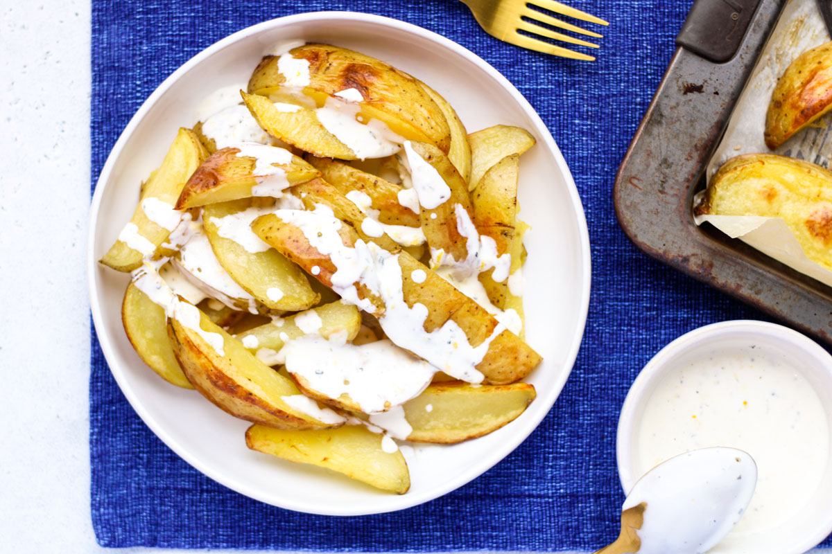 A white plate with oven roasted potatoes and yogurt sauce.