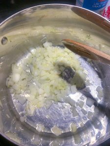 Chopped onions and garlic in a large pot with oil being stirred by a wooden spoon