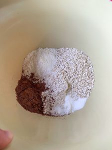 A mixing bowl filled with quinoa flakes, baking soda, cocoa powder, coconut flour, oat flour and salt