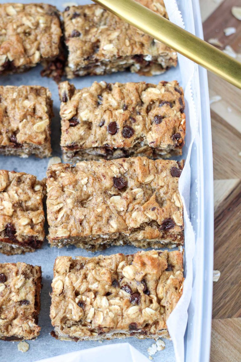 Gluten-Free Oatmeal Breakfast Bars with Chocolate in a plastic container on a wood cutting board.