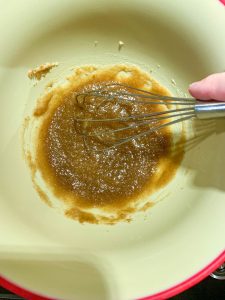 A mixing bowl with a whisk creaming applesauce and brown sugar together