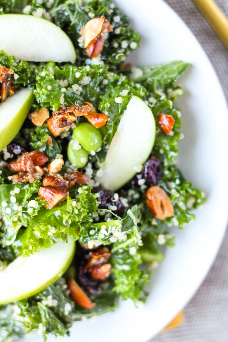 Kale salad with nuts and apple on a white plate.